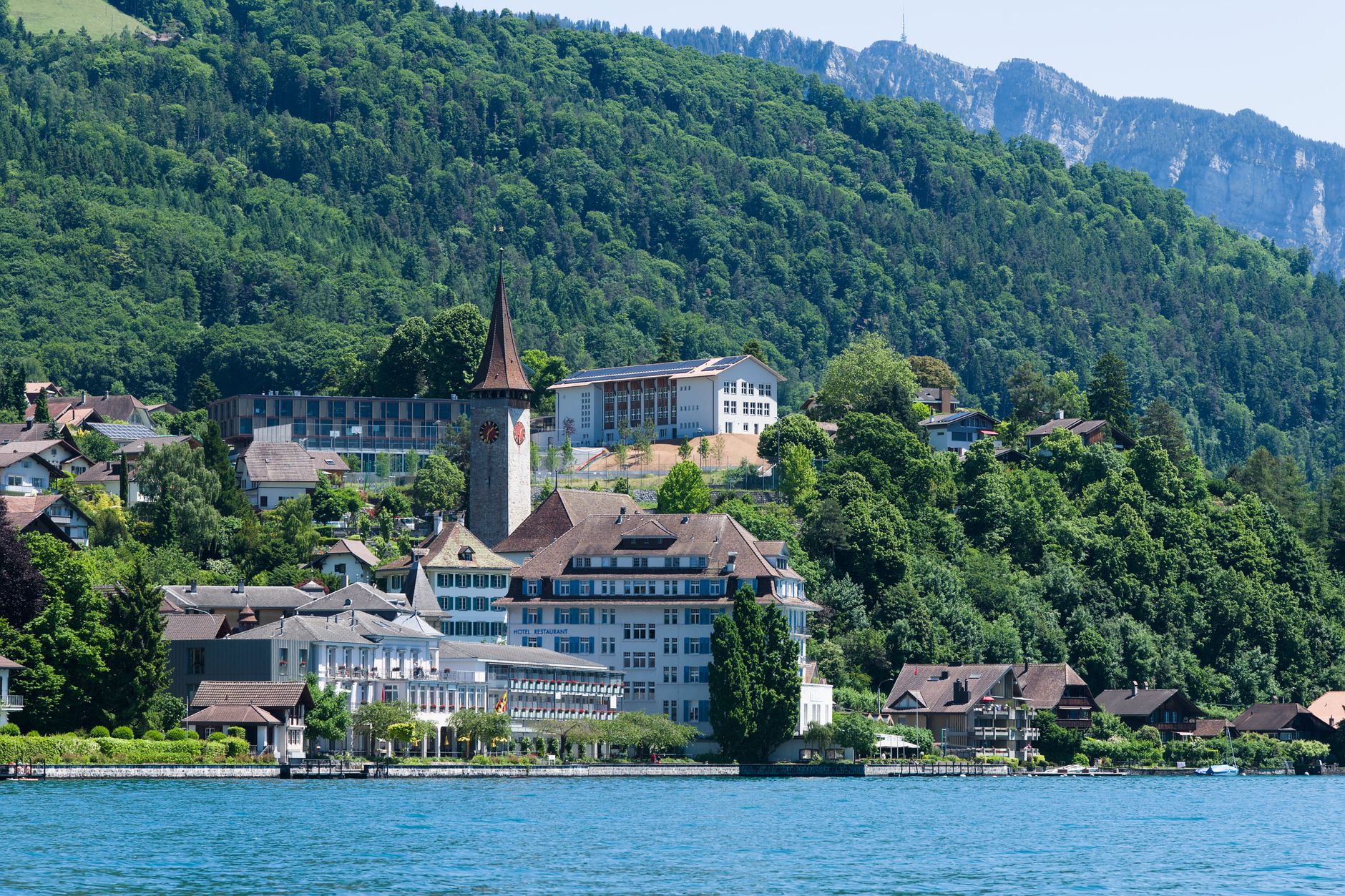 Charming Spiez village with the iconic church tower by Lake Thun, surrounded by lush green landscape and mountains.