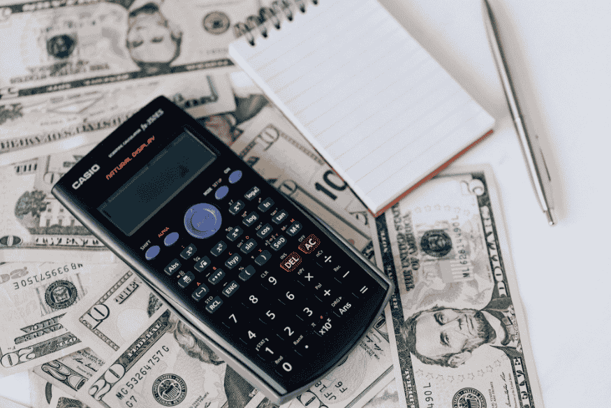 Financial calculator, notebook and pen on US dollar bills for freelancers tracking income and expenses