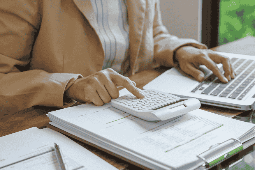 Person reviewing credit card statements with a laptop and calculator to calculate credit card interest charges.