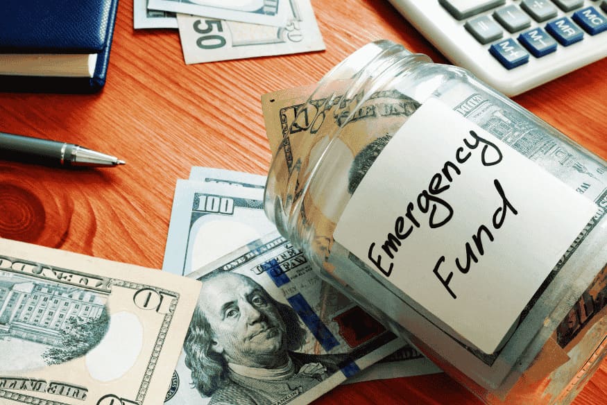 Cash on a table next to a jar labeled emergency fund.