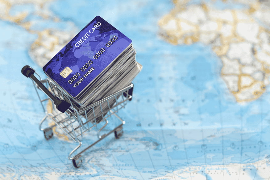 Stack of credit cards in a shopping cart on a world map, representing different travel and rewards credit card options.