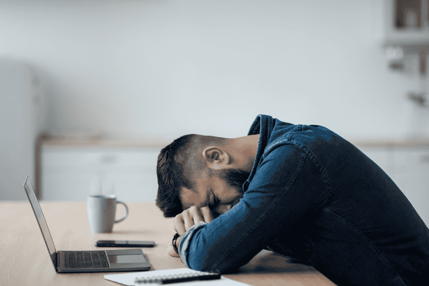 Stressed young adult at a laptop facing debt from money mistakes in his 20s.