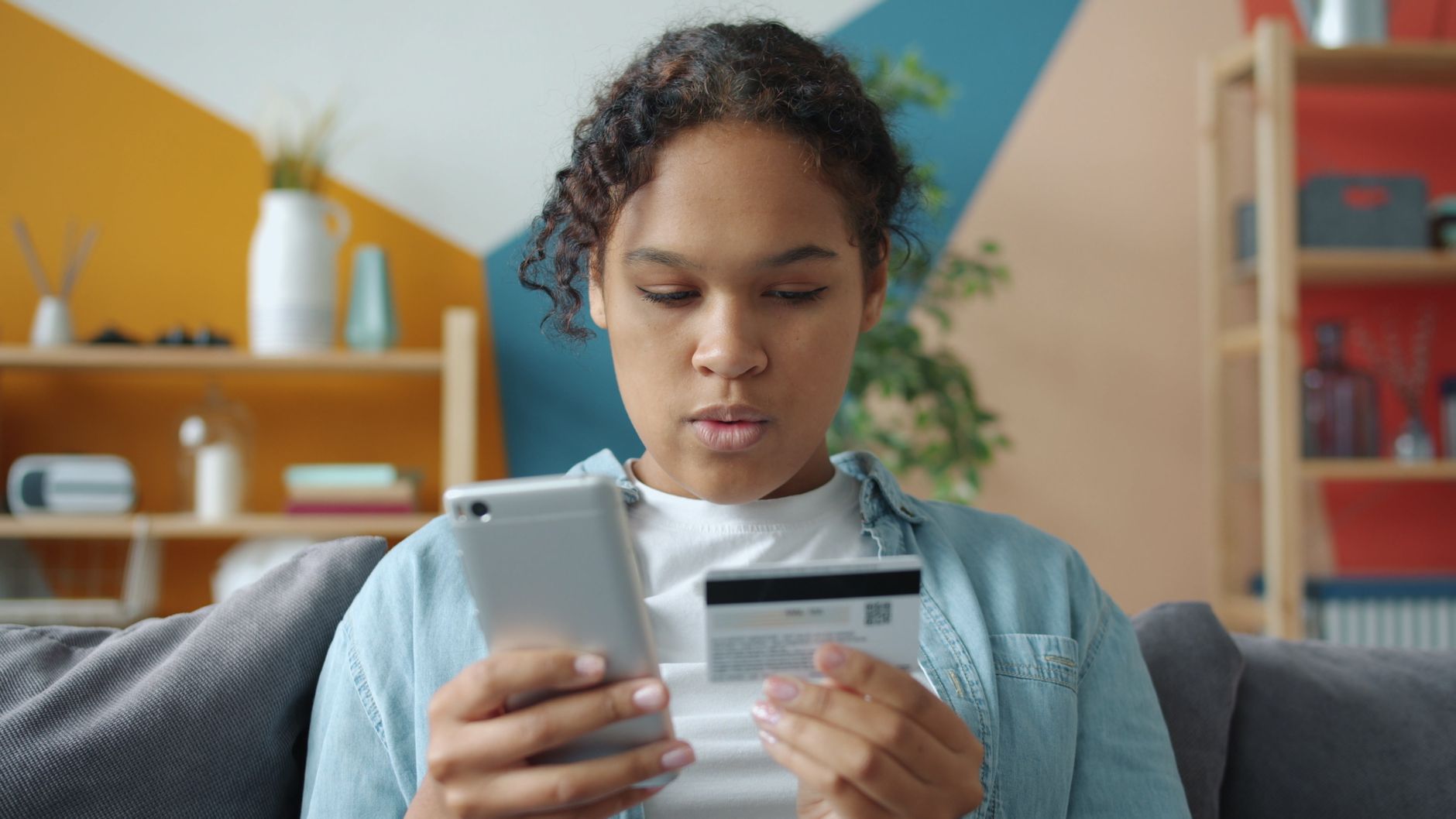 Young woman making online purchase using smartphone and credit card at home.