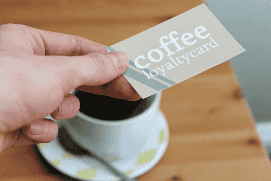 Hand holding a coffee shop loyalty card above a cup, combining store rewards with a credit card rewards strategy.