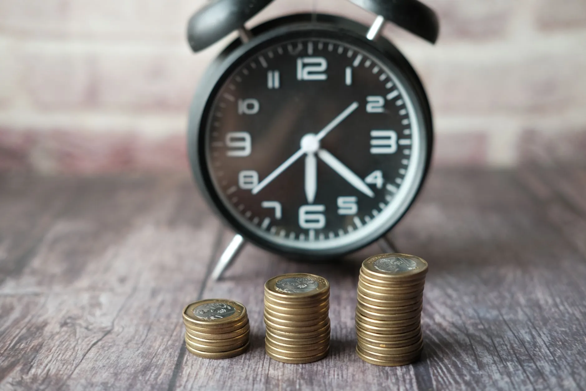Stacked coins and a classic alarm clock symbolize the value of time and money.