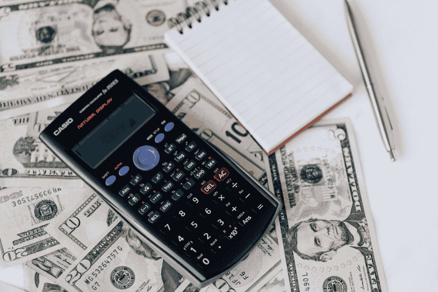 Calculator and notepad placed on top of dollar bills, representing financial planning and budgeting strategies.
