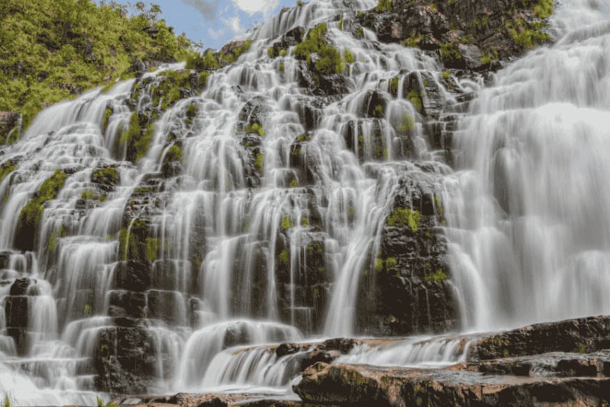 Cachoeira com várias quedas em degraus de pedra cobertos por vegetação