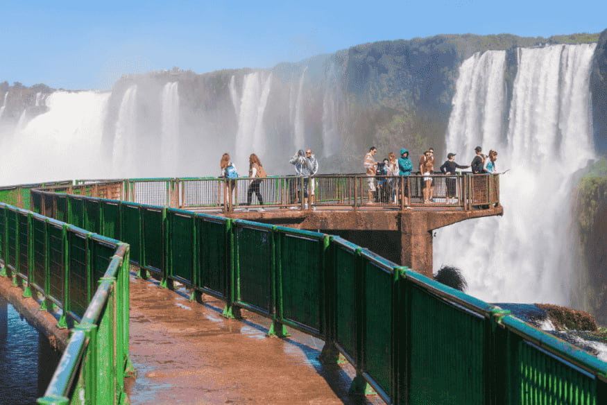 Turistas sobre passarela com vista para as quedas das Cataratas do Iguaçu.