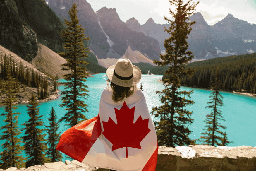 Mulher enrolada em bandeira canadense observando o Lago Moraine entre as montanhas