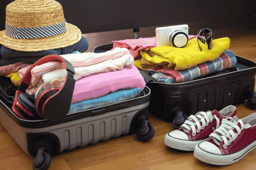 Roupas dobradas e organizadas em malas de mão com chapéu e calçados ao lado