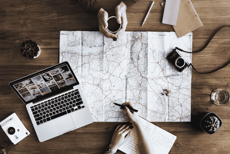 Mapa aberto sobre mesa com laptop, câmera e anotações