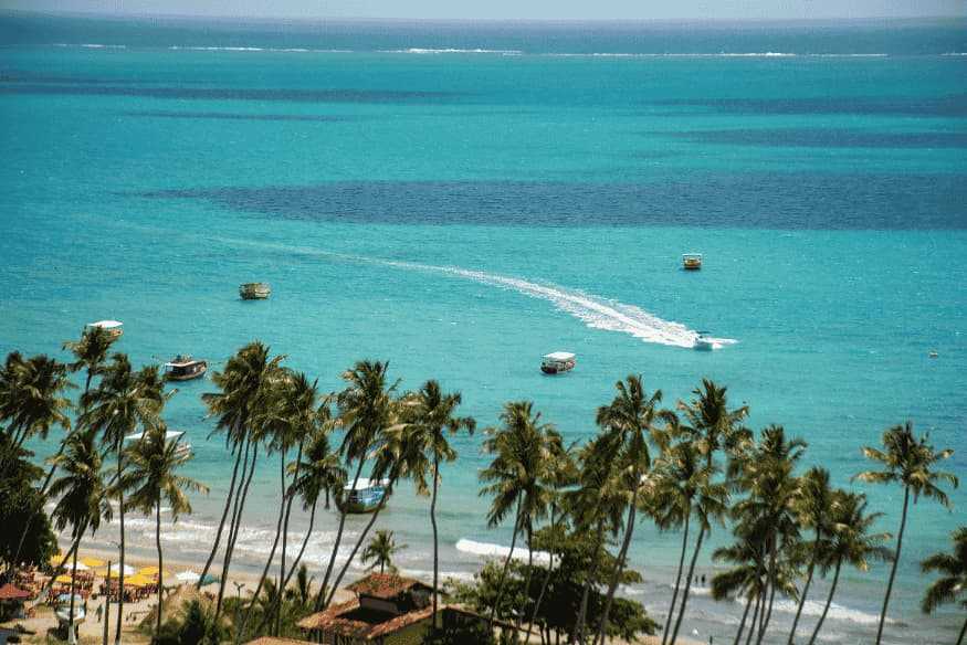 Vista do mar azul de Maragogi com barcos e coqueiros ao fundo