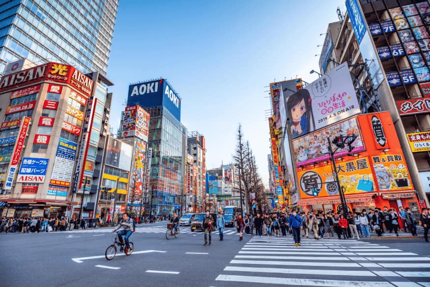 Cruzamento movimentado e colorido no bairro de Akihabara, com letreiros luminosos e pedestres.