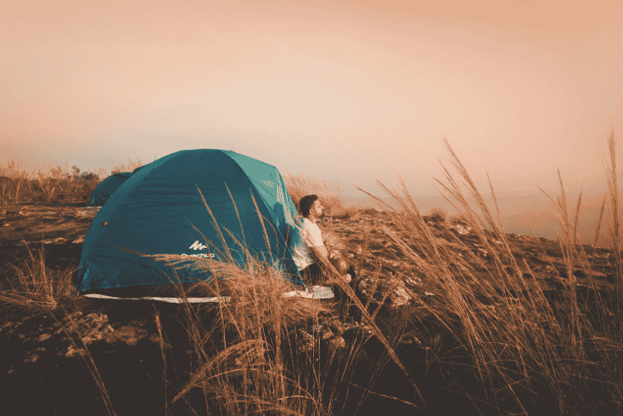 Viajante solitário ao lado de uma barraca de camping no alto de uma montanha ao pôr do sol.