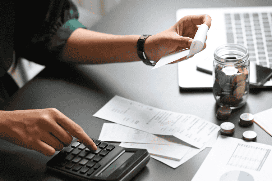 Person reviewing receipts and using a calculator to manage monthly expenses for a budget plan.