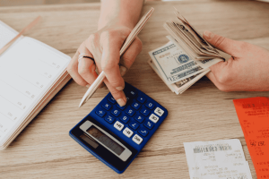 Person using a calculator and counting cash while organizing side income earnings.