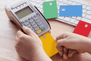 Hand inserting a credit card into a payment terminal with other cards on the desk.