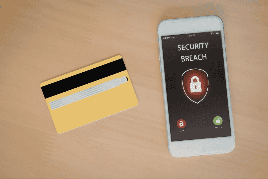 Smartphone showing security breach alert next to credit card, symbolizing credit card fraud prevention