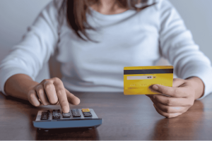 Woman holding a credit card while using a calculator to understand how credit card interest is calculated.