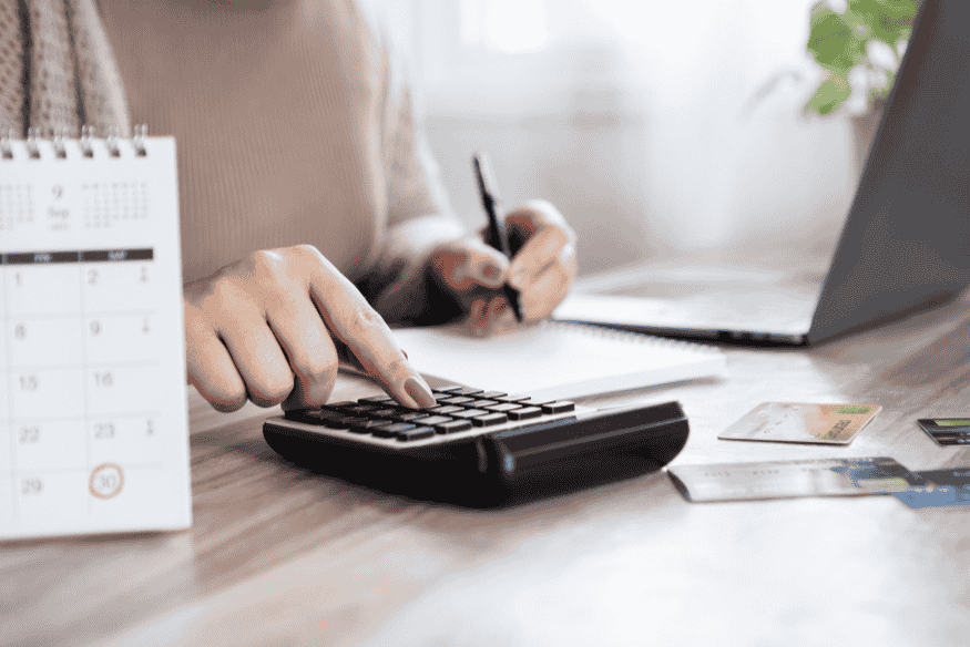 Person using a calculator and laptop to track credit card rewards and payment due dates.