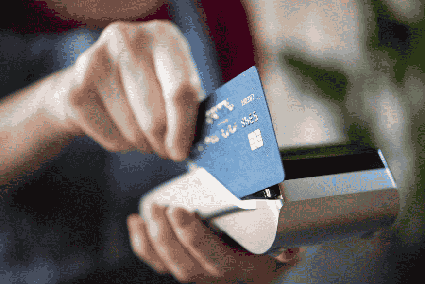Person tapping a blue credit card on a payment terminal, illustrating everyday credit card transactions.