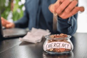 Person putting coins into a glass jar labeled emergency to build an emergency fund