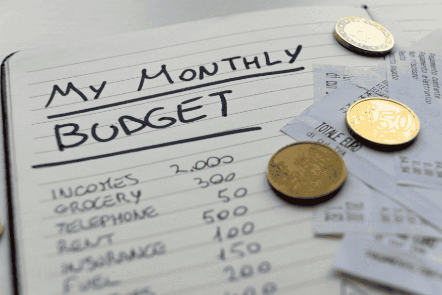 Monthly budget notebook with expenses listed and coins and receipts on top
