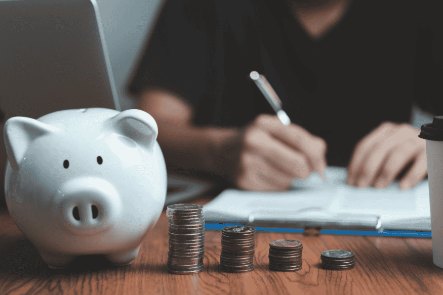 White piggy bank and stacks of coins in front of a person planning their savings