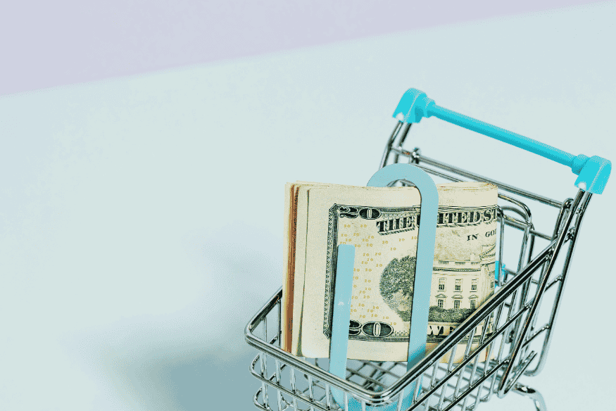 Small shopping cart filled with U.S. dollar bills representing how freelancers price their services to meet financial goals.