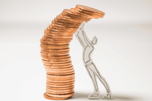 Paper figure supporting a leaning stack of coins symbolizing fragile financial surplus