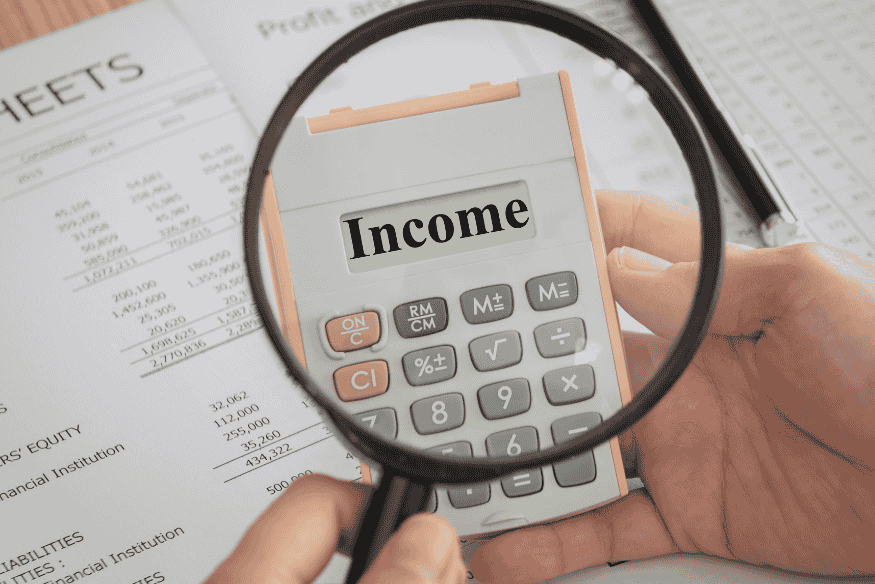 Magnifying glass focusing on the word income on a calculator to track irregular paychecks