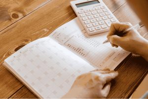 Using a planner and calculator to schedule bills and savings goals in a monthly budget plan