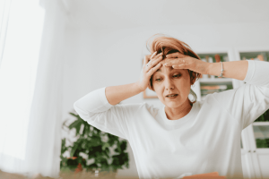 Stressed woman holding her head in her hands at home, representing the emotional toll of overspending and money anxiety.