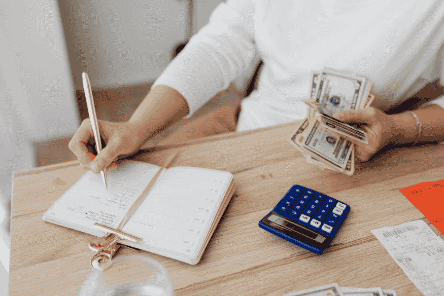 Person holding cash and writing in a budget notebook with calculator to manage spending calmly