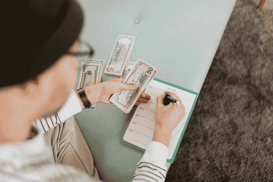 Person counting cash and writing in a weekly planner to control personal expenses without stress