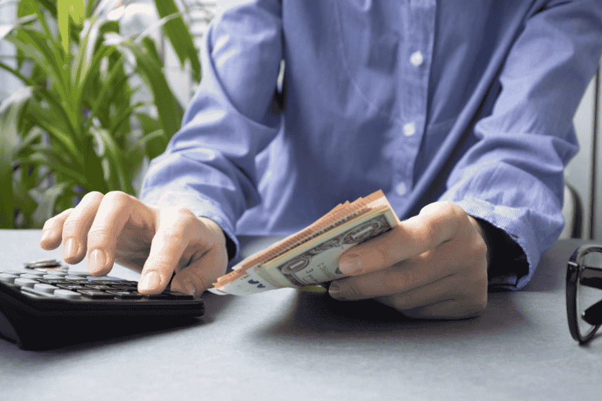 Business owner counting cash and logging numbers in a calculator to keep work money separate from personal money