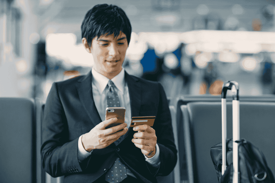 Business traveler at airport using smartphone and travel credit card to manage trip expenses